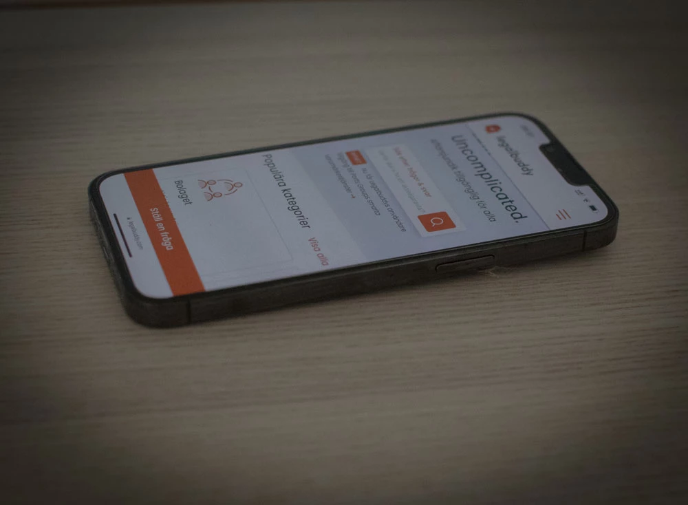 En mobiltelefon med Legalbuddys hemsida ligger på ett bord.